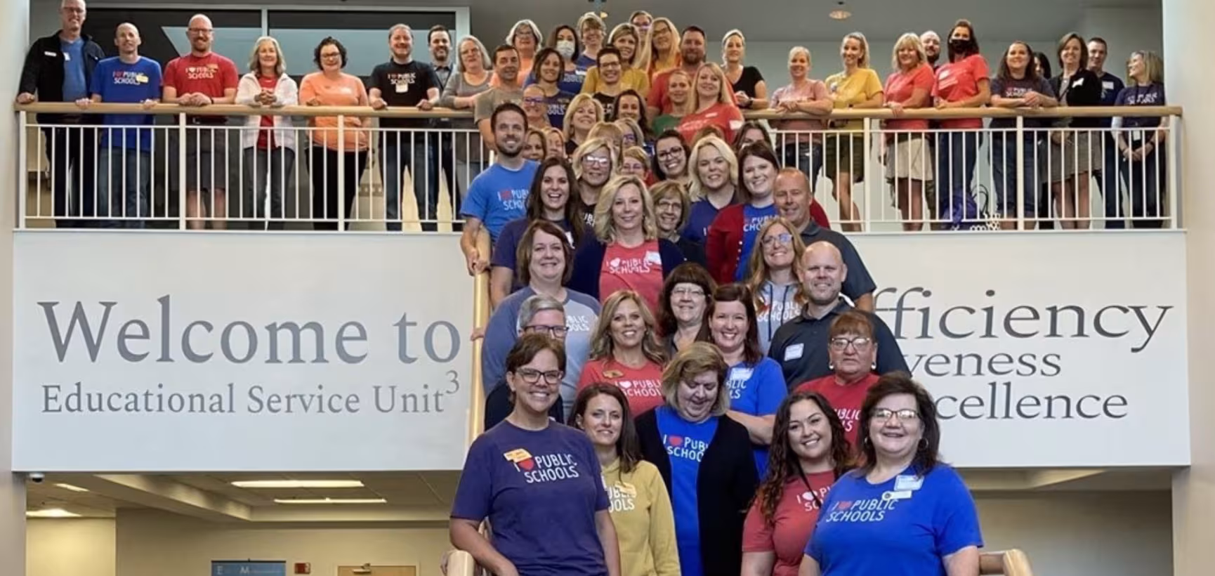 An image of ESU personnel from across Nebraska fill a staircase and the adjacent balcony. They are on the steps at ESU 3 and  ESU 3's branding and wall decor of their member districts adorn the walls.